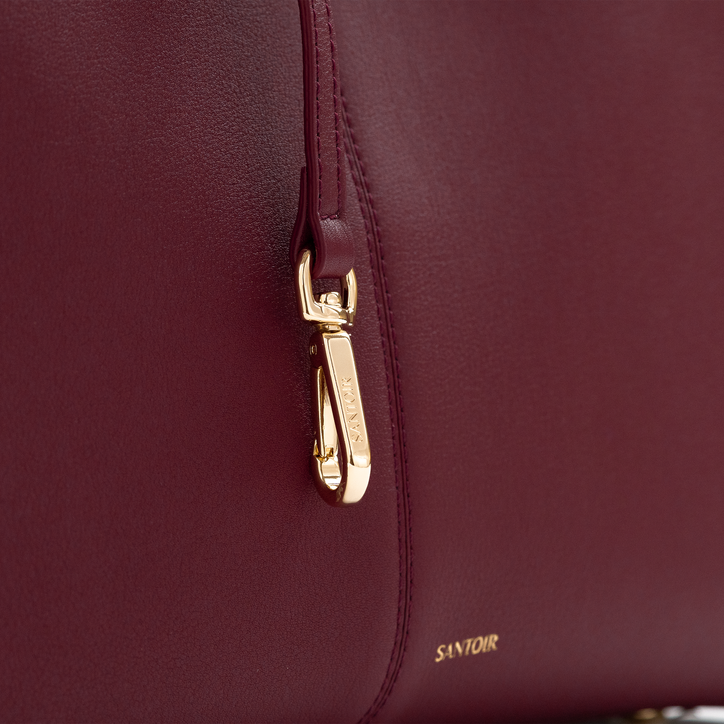 Close-up of buttery soft bordeaux calfskin leather with gold hardware and hand-finished stitching, luxury craftsmanship by Santoir.