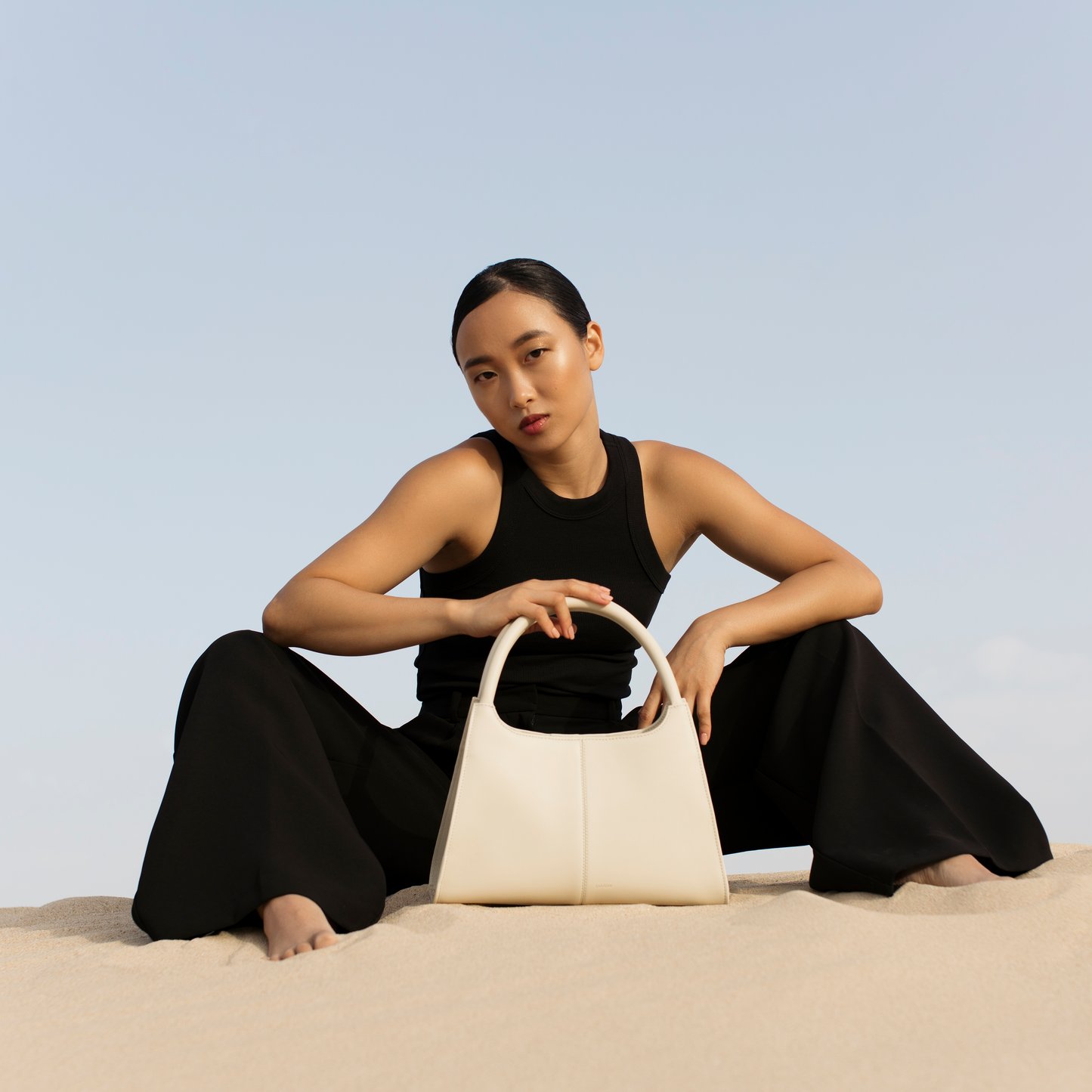 Elegant ivory smooth leather handbag styled on model, structured trapezoid silhouette in soft neutral calfskin, Santoir Classic 5 for modern women.
