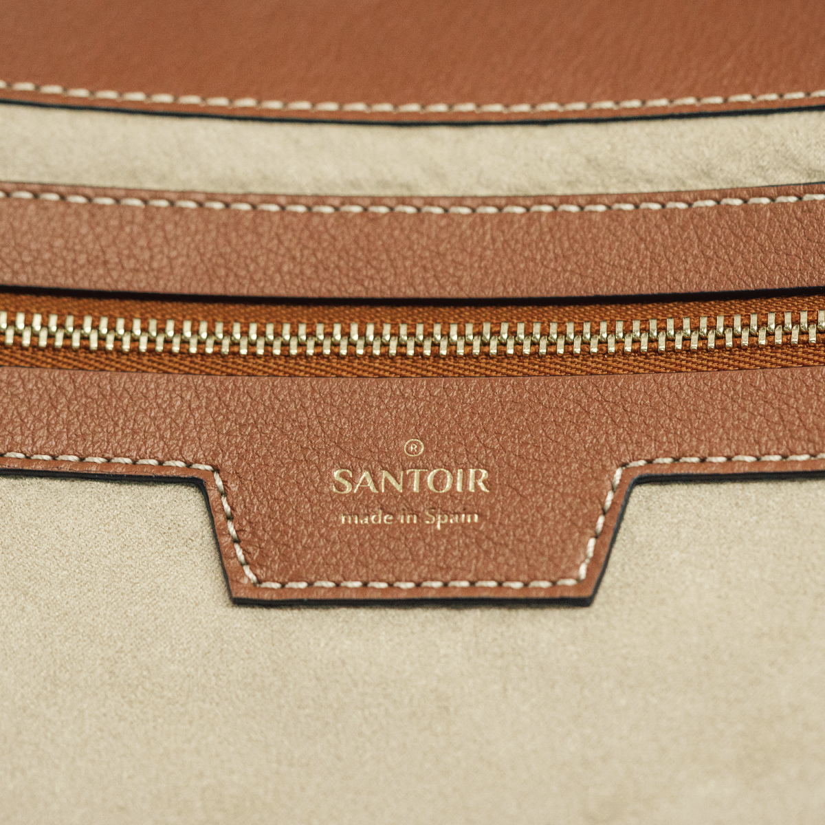 Close-up of Santoir logo embossed in gold on smooth caramel brown calfskin leather interior, showcasing fine craftsmanship and luxury handbag details made in Spain.