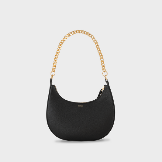 Black leather crescent handbag with  gold chain shoulder strap, featuring a structured silhouette and a secure zip closure. Santoir Luna bag in pebbled leather, convertible from everyday wear to elegant evening bag, handcrafted in Spain