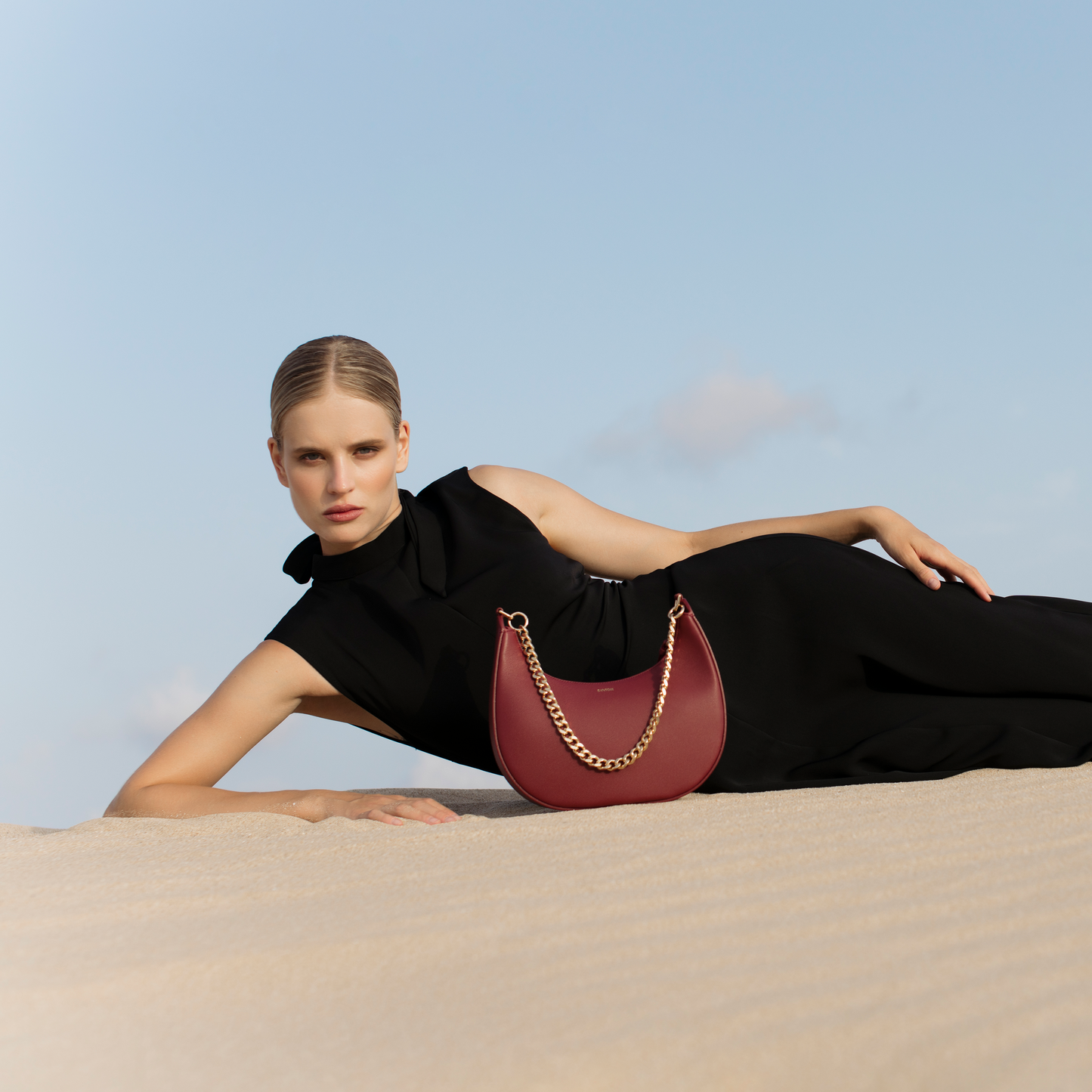 Elegant deep red crescent moon bag worn by model with gold chain, Santoir Luna in bordeaux smooth leather, versatile from day to evening.