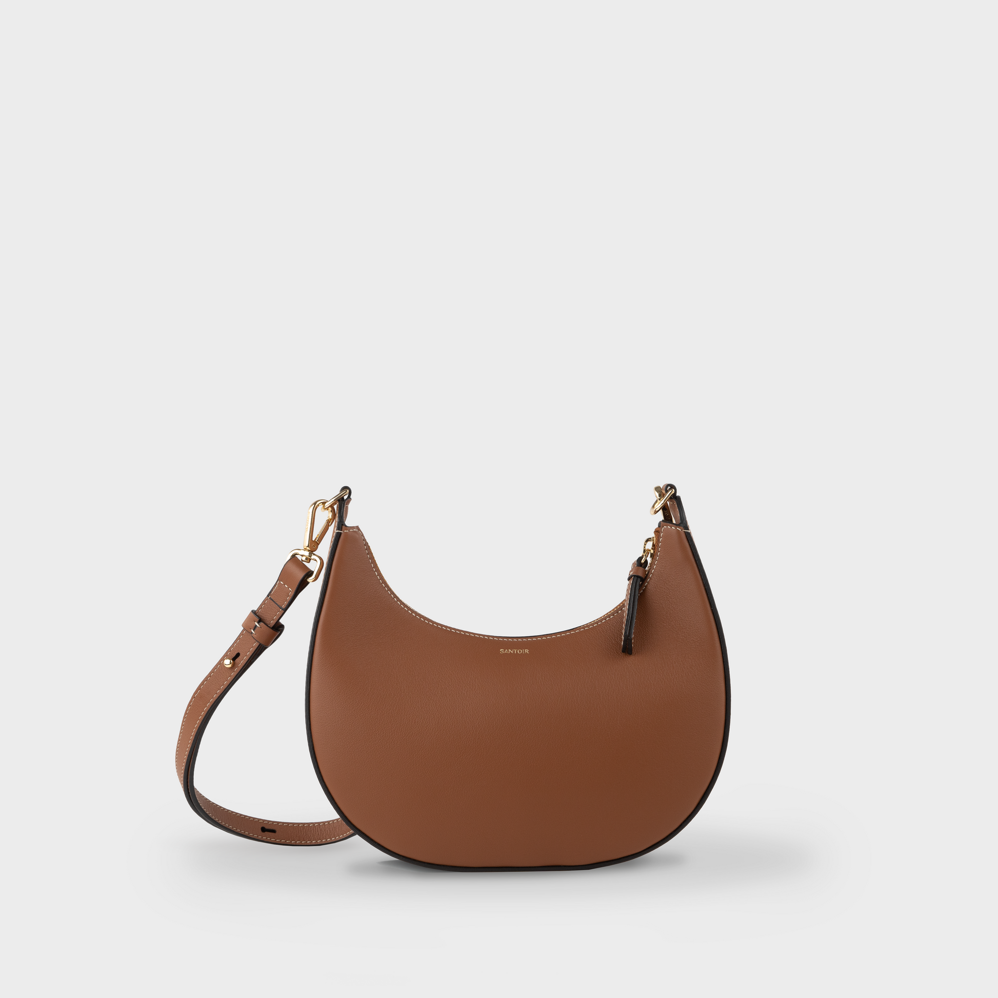 Tan crossbody crescent bag with adjustable long strap, Santoir Luna in smooth caramel calfskin, semi-structured warm brown handbag for everyday use, handcrafted in Spain.