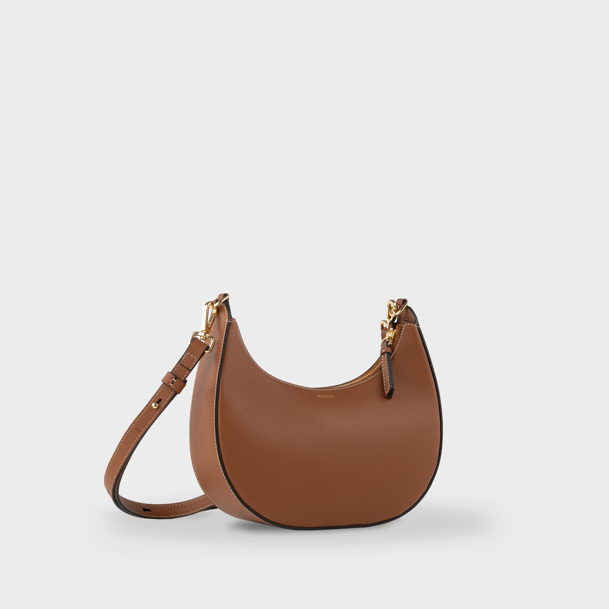 Tan crossbody crescent bag with adjustable long strap, side view of Santoir Luna in smooth caramel calfskin, semi-structured warm brown handbag for everyday use, handcrafted in Spain.