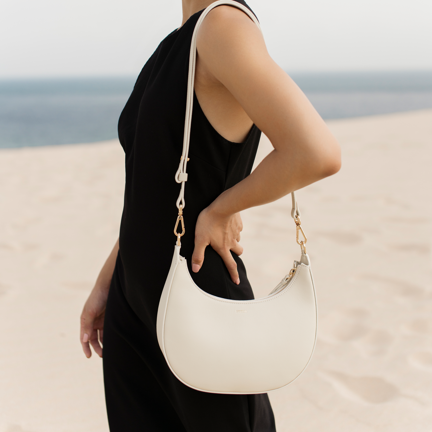 Ivory leather crescent bag styled on model with adjustable strap, neutral everyday to night bag, Santoir Luna in smooth off-white leather, minimalist and versatile.