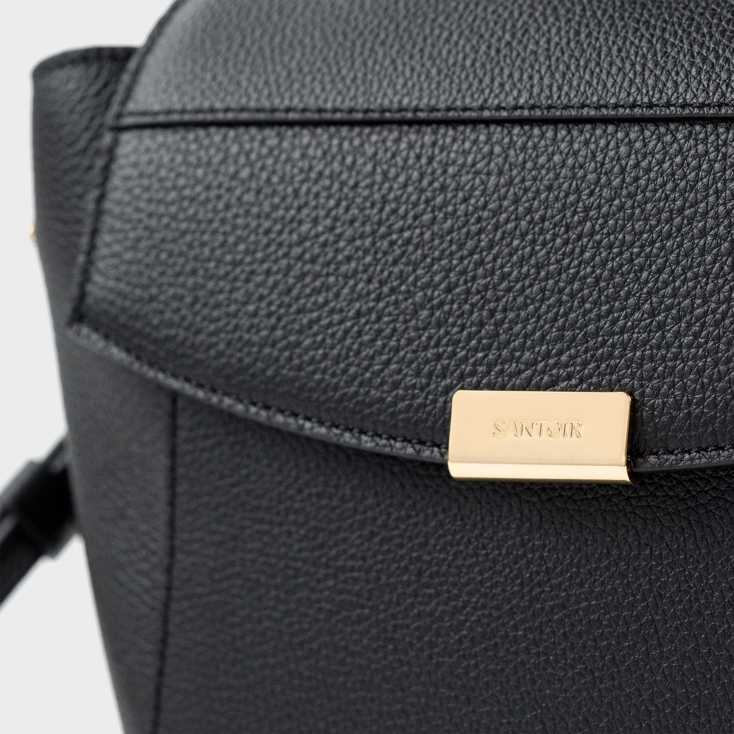 Close-up of Santoir logo in gold-tone metal on black pebbled calfskin leather, minimalist luxury branding on the structured Mini Boss handbag.
