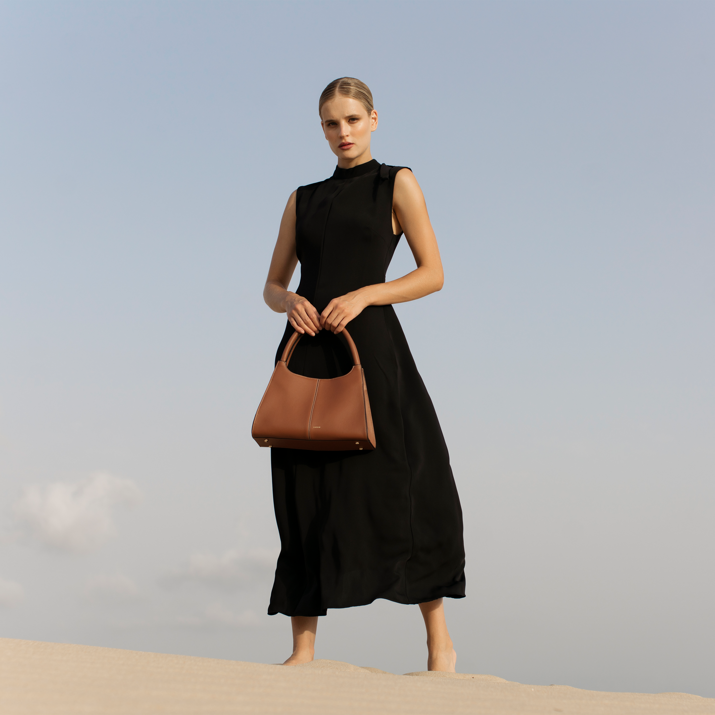 Elegant caramel brown leather handbag styled on model’s hands, timeless trapezoid silhouette with structured shape, Santoir Classic 5 bag for modern women.